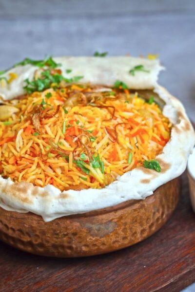 A flavorful bowl of homemade biryani served with raita, lemon, and tomato on the side.