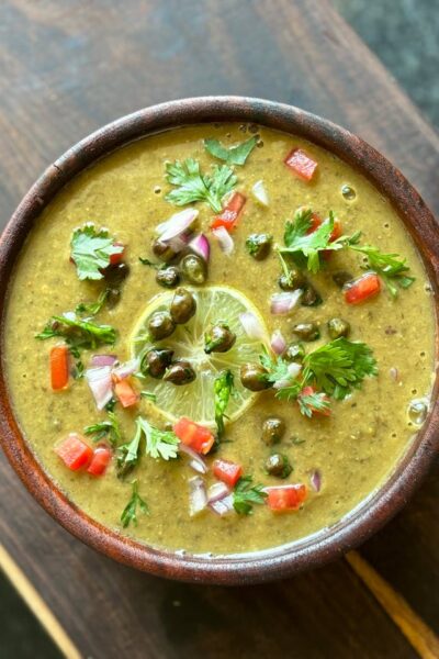 A vibrant bowl of traditional Indian lentil soup garnished with fresh coriander, chili, and lime.
