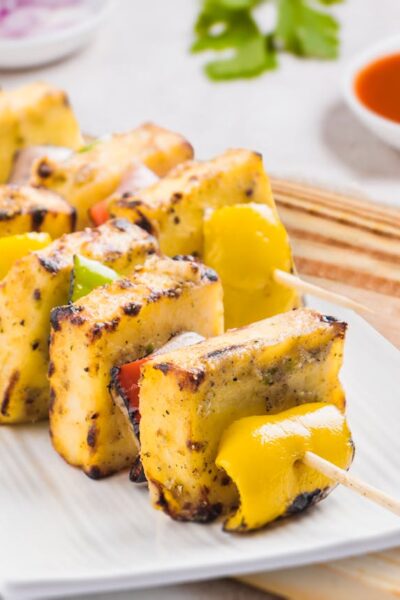 Tasty grilled paneer tikka skewers served on a plate with sauces, perfect for an Indian cuisine experience.