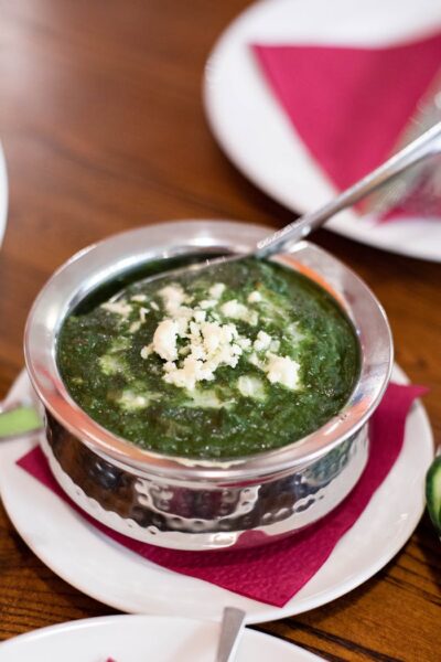Top-down view of creamy palak paneer served in a stainless steel bowl, garnished with crumbled cheese.